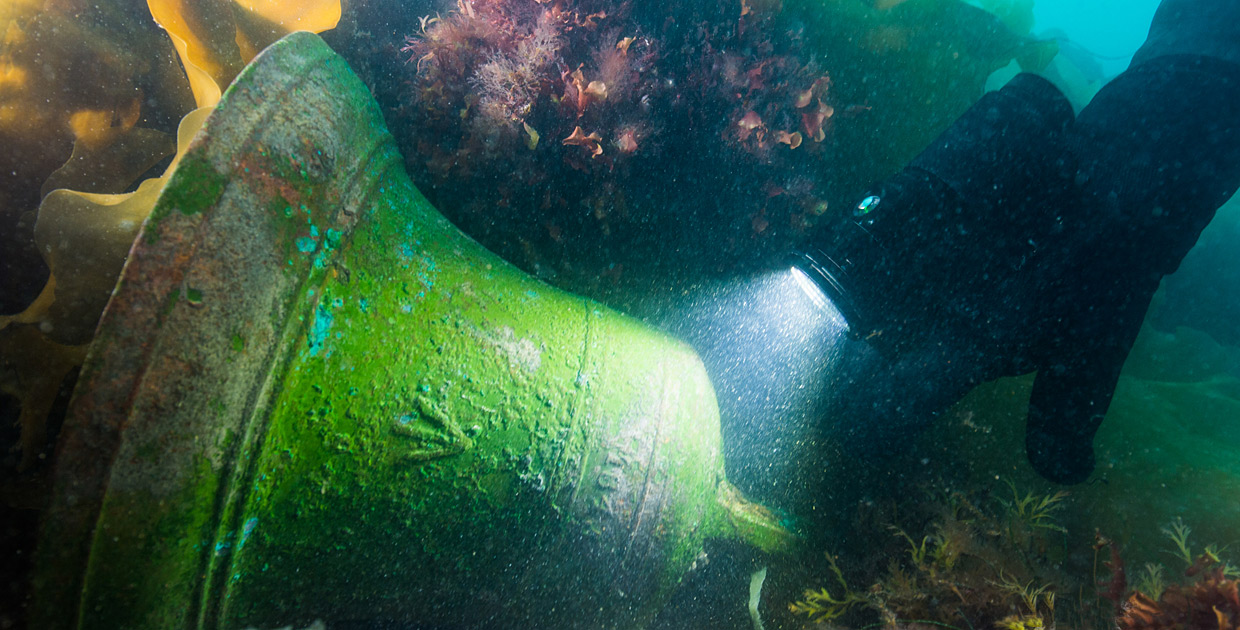 A person in a wetsuit is looking at a bell in the water at the Canadian Museum of History.