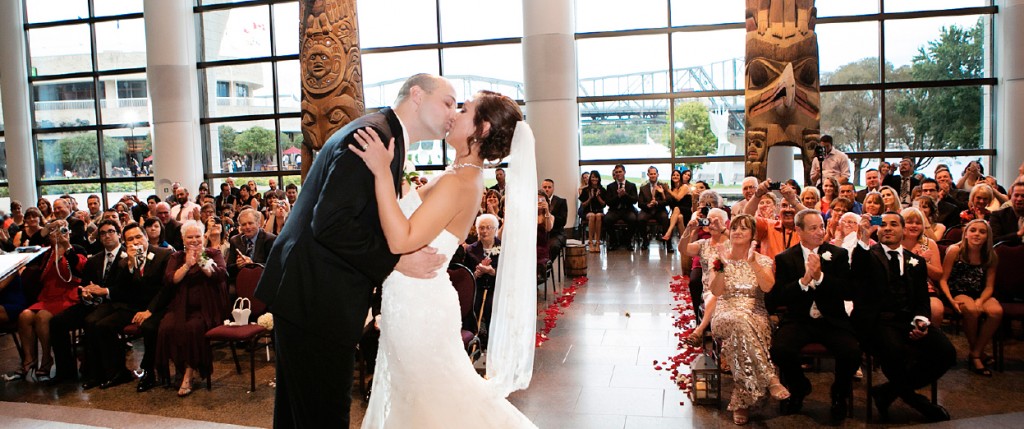 A bride and groom kissing in front of a large crowd at the Canadian Museum of History in Ottawa.