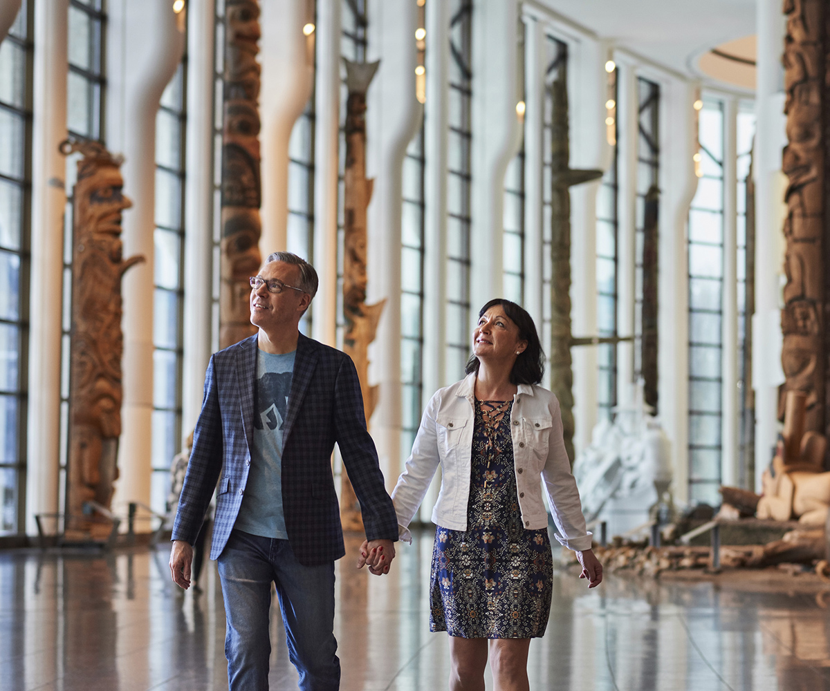 A man and woman walking through the Canadian Museum of History in Ottawa, admiring totem poles.