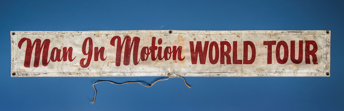 A man in motion world tour sign hanging on a blue wall at the Canadian Museum of History in Ottawa.