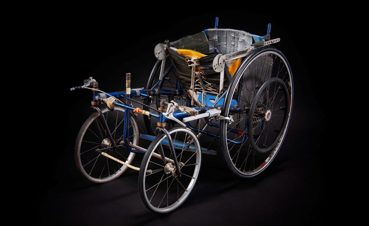 An image of a wheelchair with wheels on a black background, displayed at the Canadian Museum of History in Ottawa.