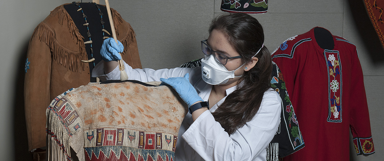 A woman wearing a mask and gloves inspecting a piece of clothing at the Canadian Museum of History in Ottawa.