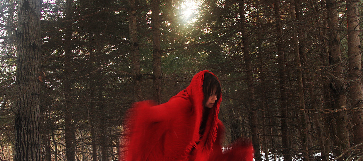 A person wearing a red hooded cloak in the woods in Ottawa.