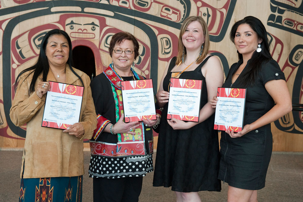 Four women holding certificates in front of a totem pole at the Canadian Museum of History in Ottawa.