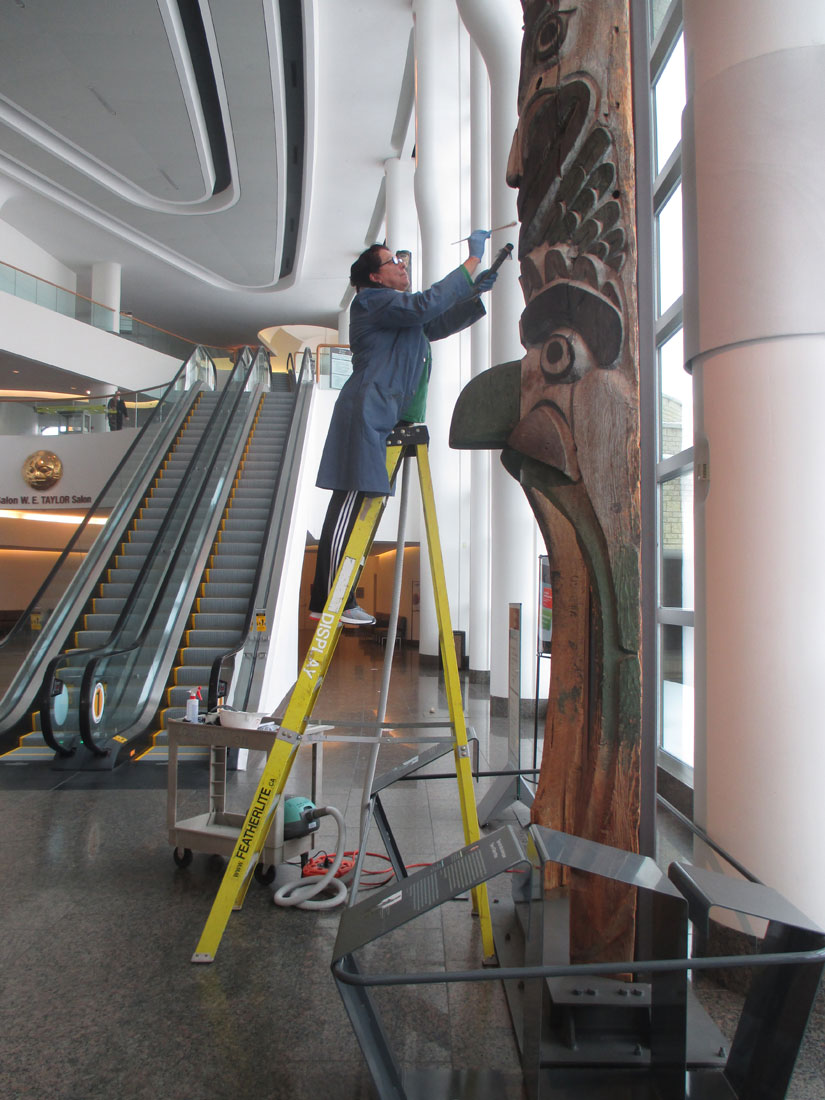 A woman on a ladder working on a totem pole at the Canadian Museum of History in Ottawa.