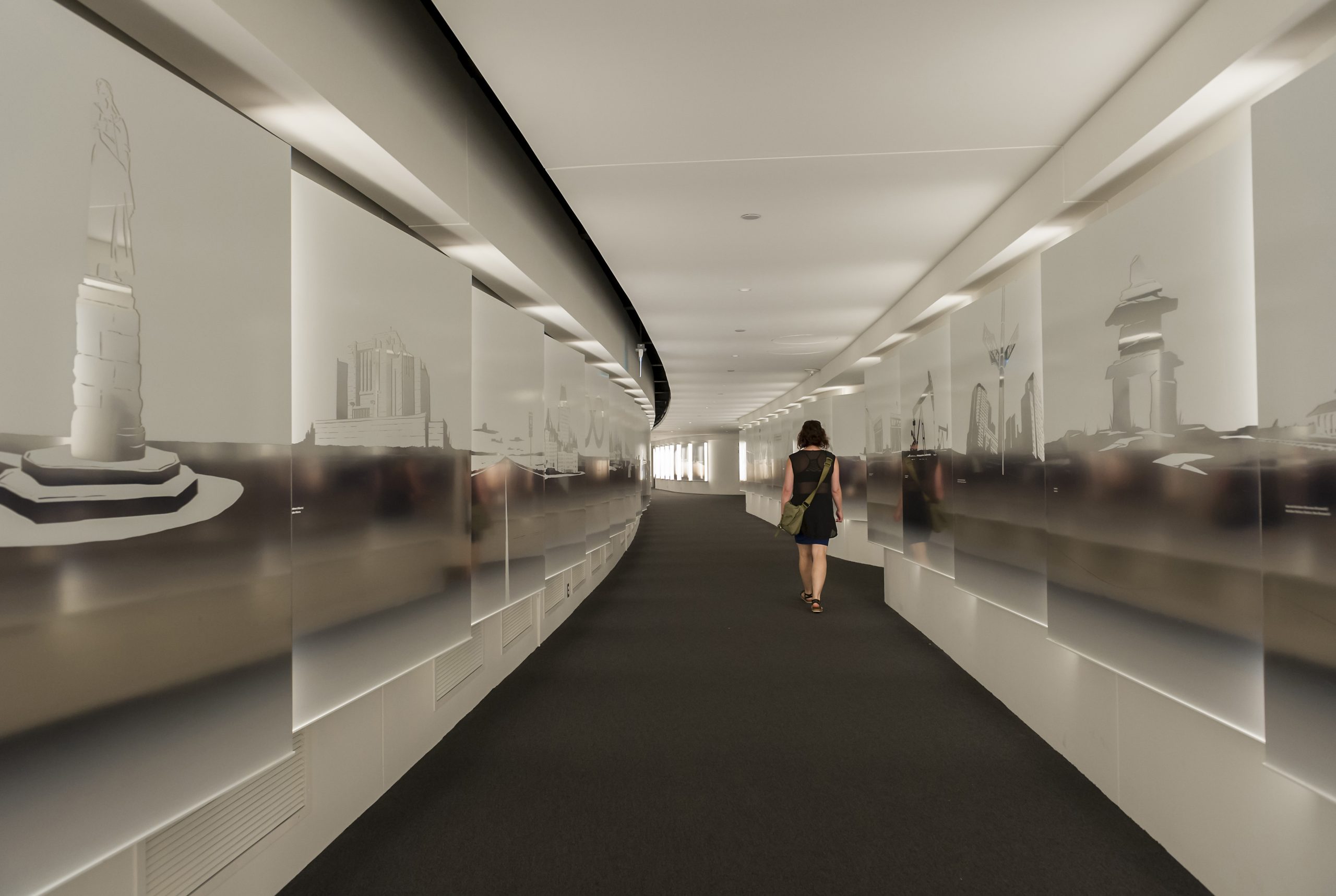 A woman is walking down a hallway with pictures on the wall at the Canadian Museum of History.